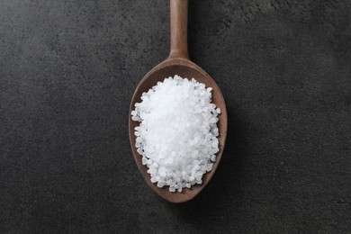 Photo of Natural salt in wooden spoon on dark grey table, top view