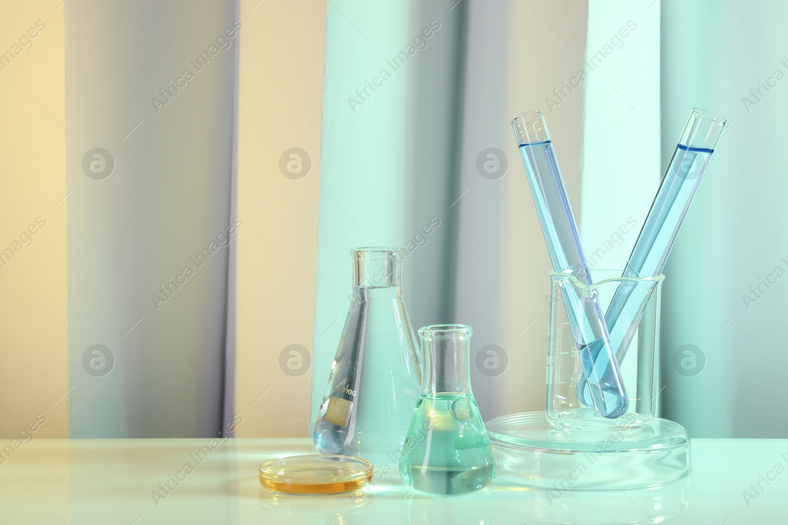 Photo of Laboratory analysis. Different glassware on table against color background, space for text