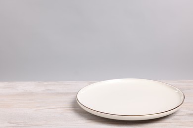 Photo of Empty ceramic plate on wooden table against light background, space for text