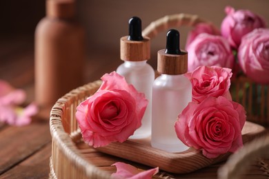 Photo of Tray with bottles of essential rose oil and flowers on wooden table, closeup