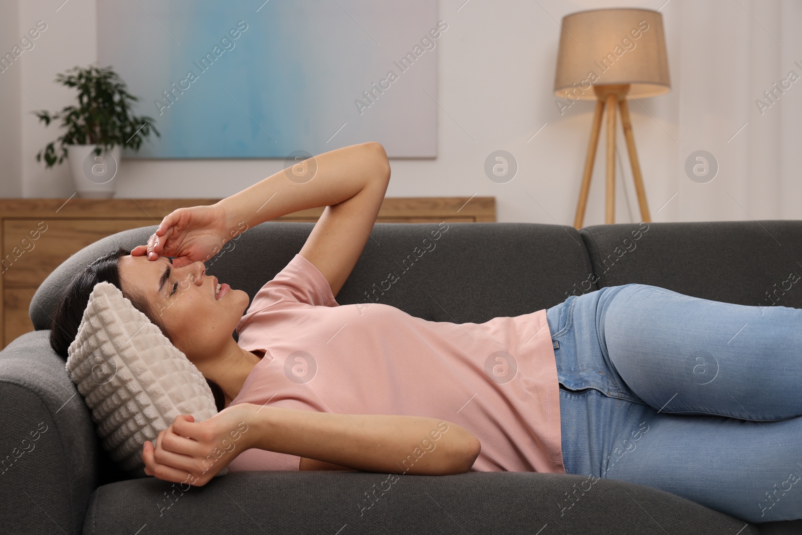 Photo of Sad woman suffering from headache on sofa indoors