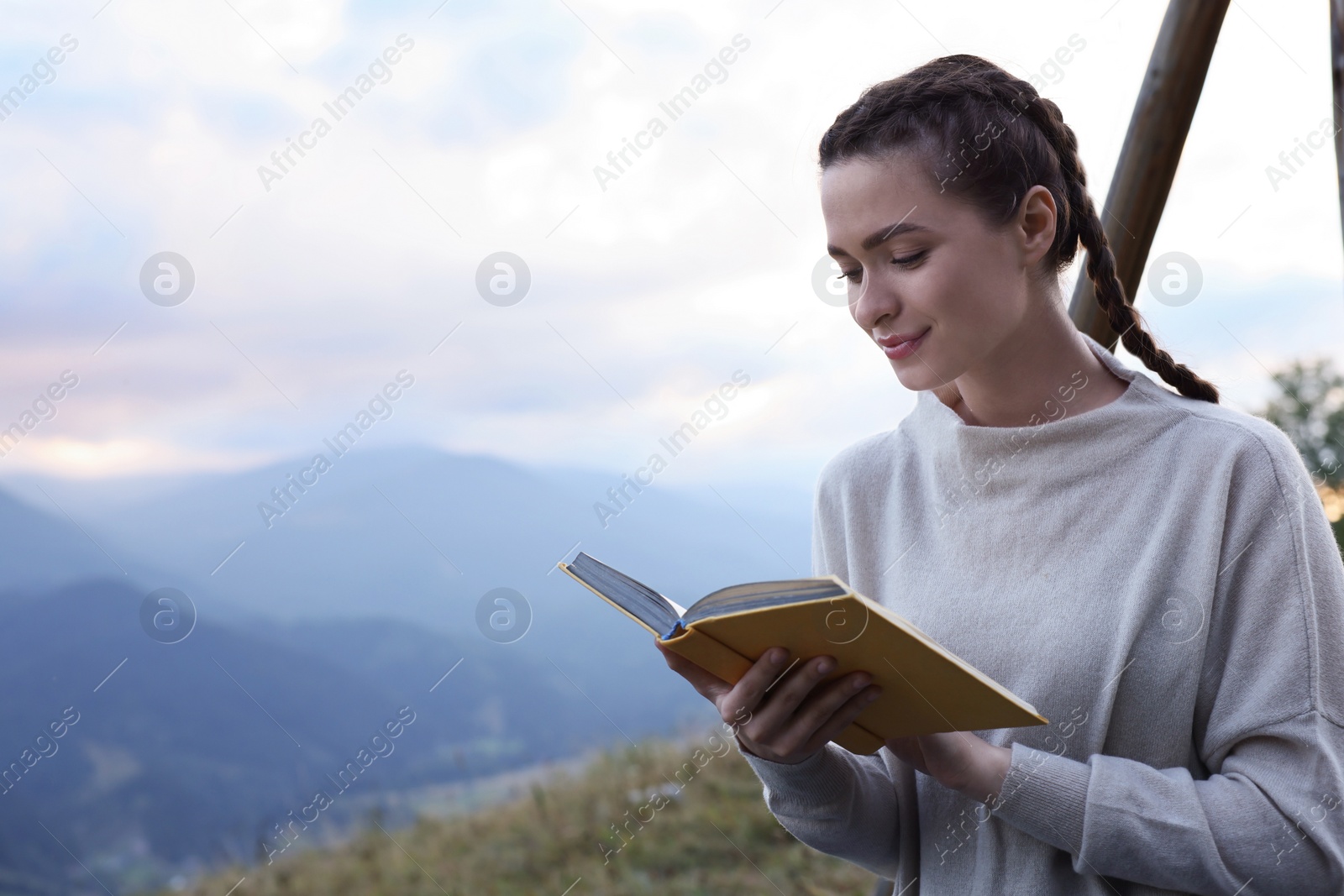 Photo of Beautiful young woman reading book in mountains, space for text