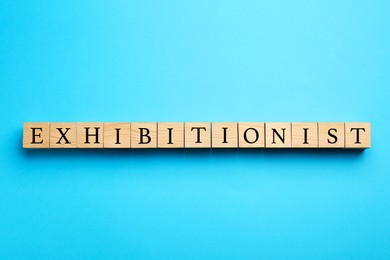 Photo of Word EXHIBITIONIST made with wooden cubes on light blue background, flat lay
