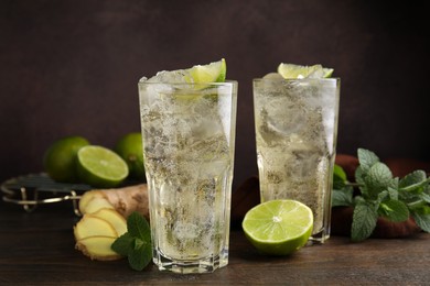 Photo of Glasses of tasty ginger ale with ice cubes and ingredients on wooden table