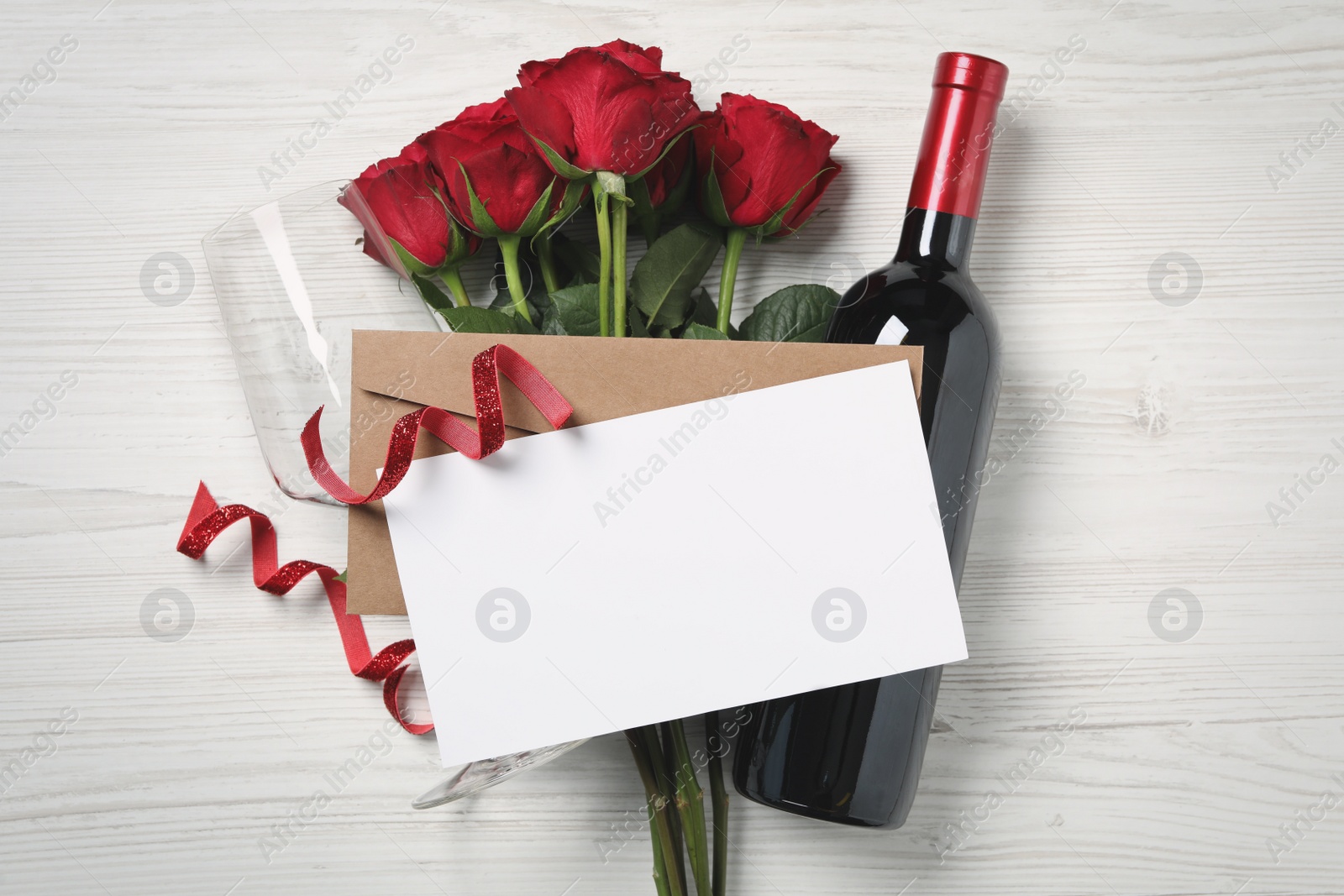 Photo of Flat lay composition with blank greeting card, wine and roses on white wooden table. Valentine's day celebration