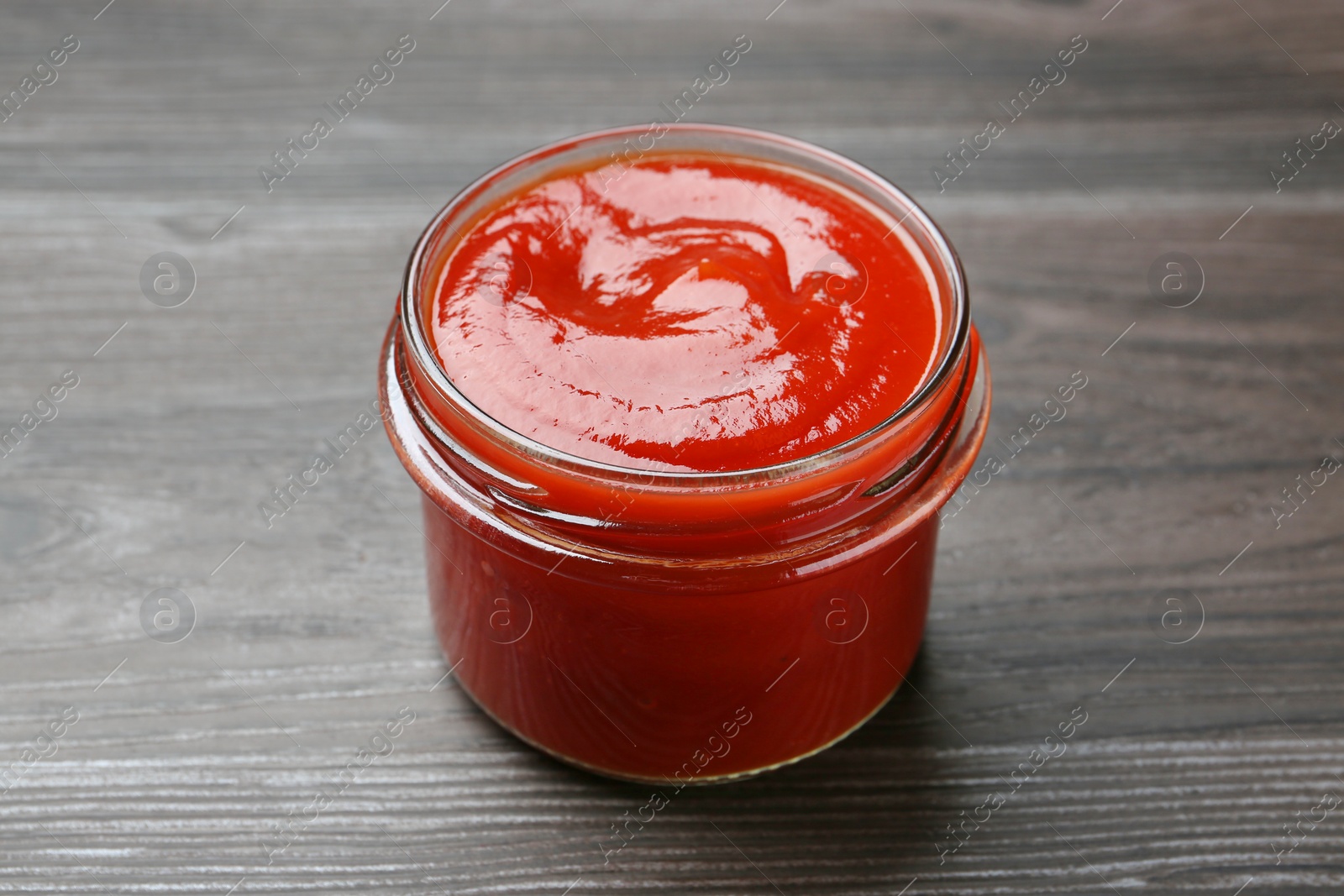 Photo of Tasty ketchup in jar on grey wooden table. Tomato sauce