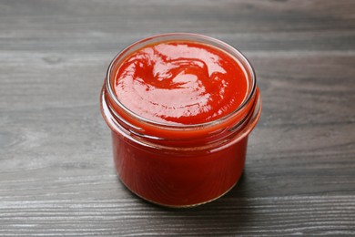 Photo of Tasty ketchup in jar on grey wooden table. Tomato sauce