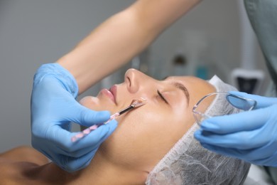 Photo of Cosmetologist applying chemical peel product on client's face in salon