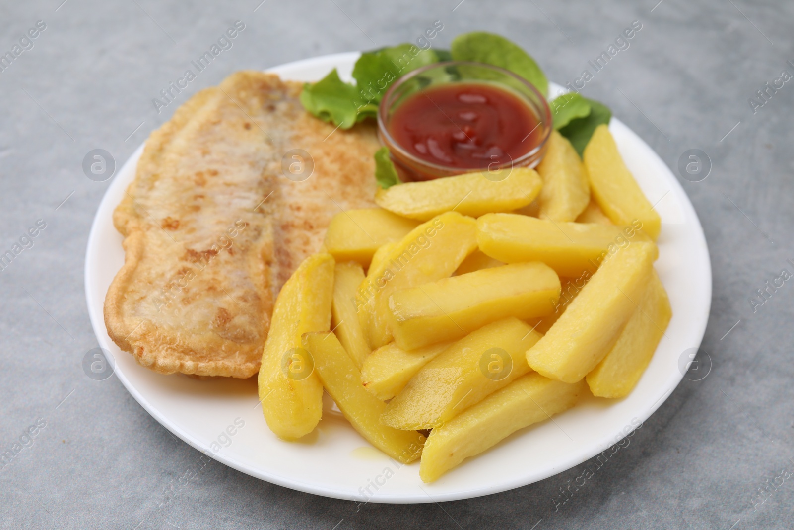 Photo of Delicious fish and chips with ketchup and lettuce on gray table, closeup