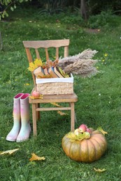 Photo of Rubber boots, chair, pumpkin and apples on green grass outdoors. Autumn atmosphere