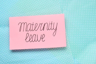 Photo of Card with phrase Maternity Leave on turquoise fabric, top view. Space for text