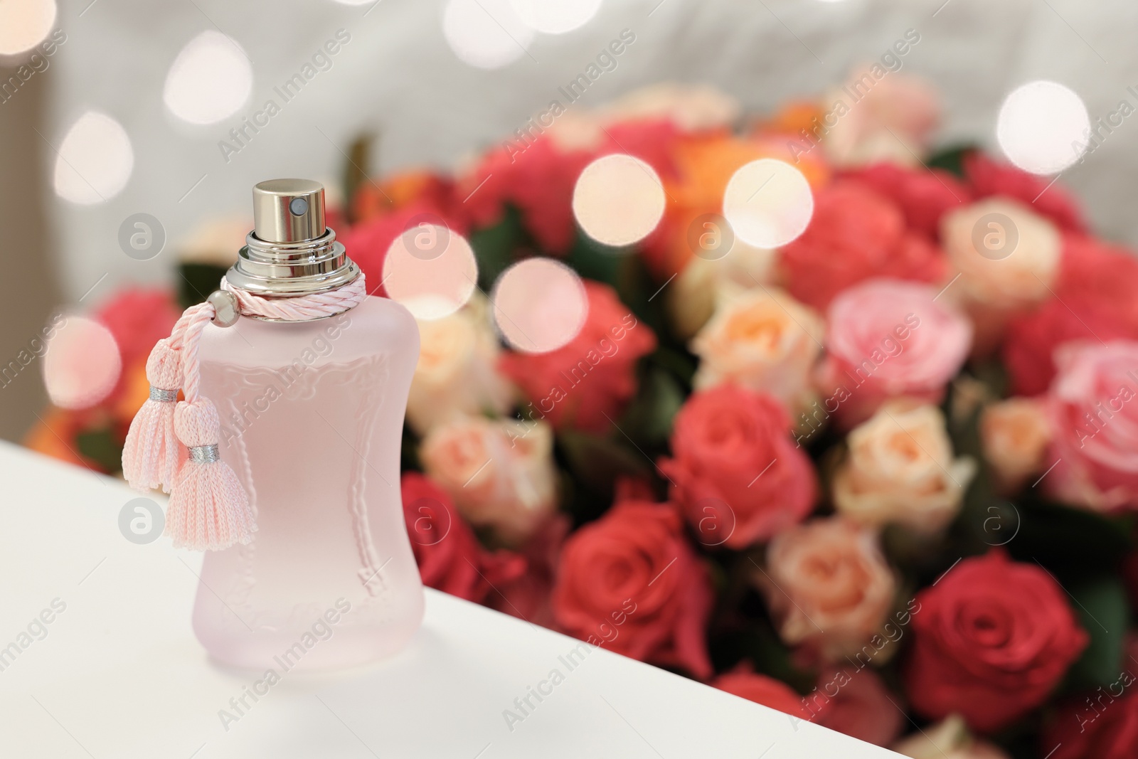 Photo of Bottle of perfume on white table against bouquet of beautiful roses. Space for text