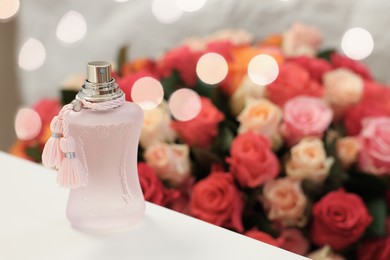 Photo of Bottle of perfume on white table against bouquet of beautiful roses. Space for text