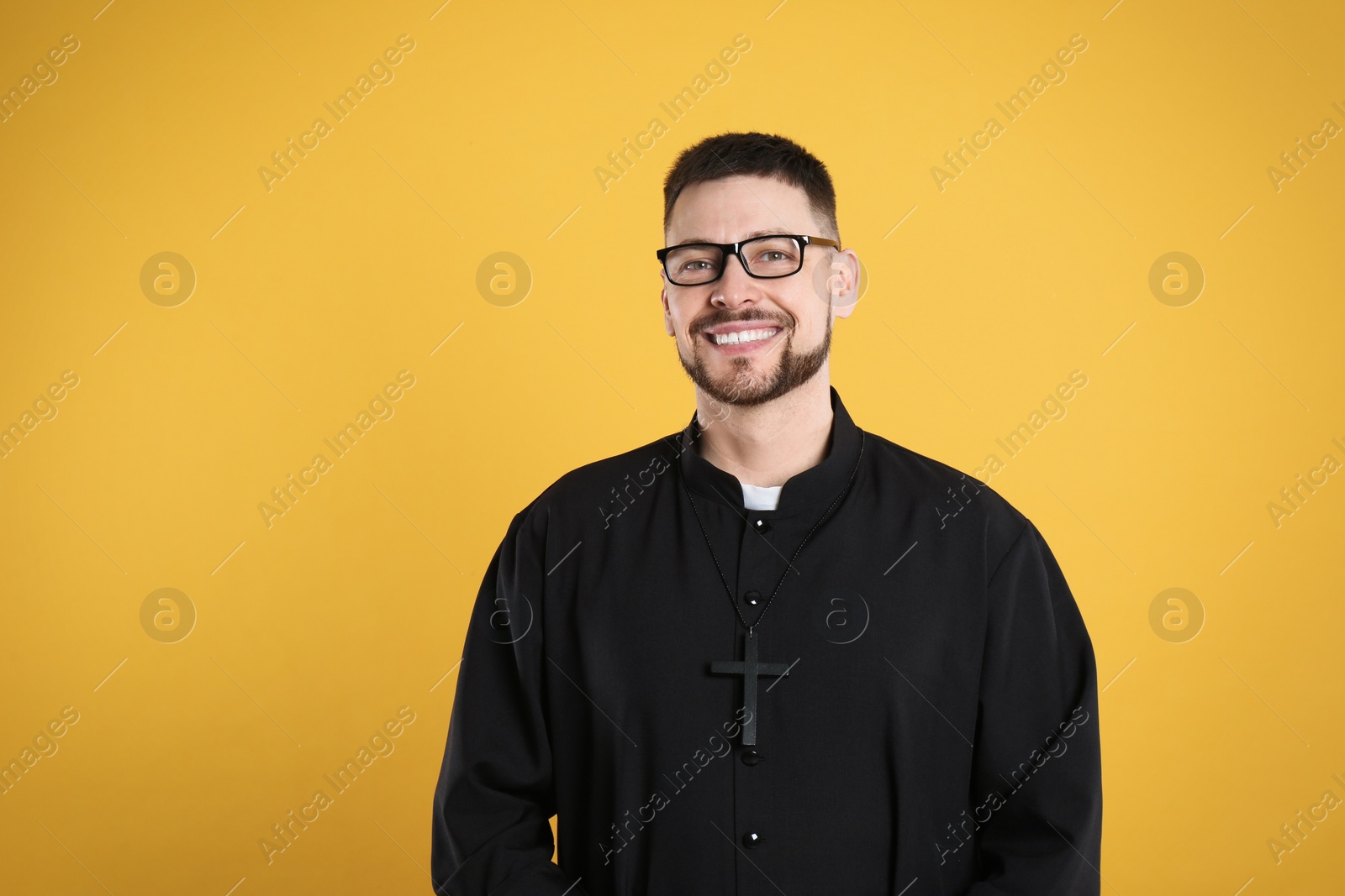 Photo of Priest wearing cassock with clerical collar on yellow background