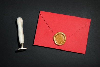 Photo of Envelope with wax seal and stamp on black background, flat lay