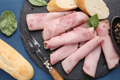 Photo of Rolled slices of delicious ham and baguette served on blue wooden table, flat lay