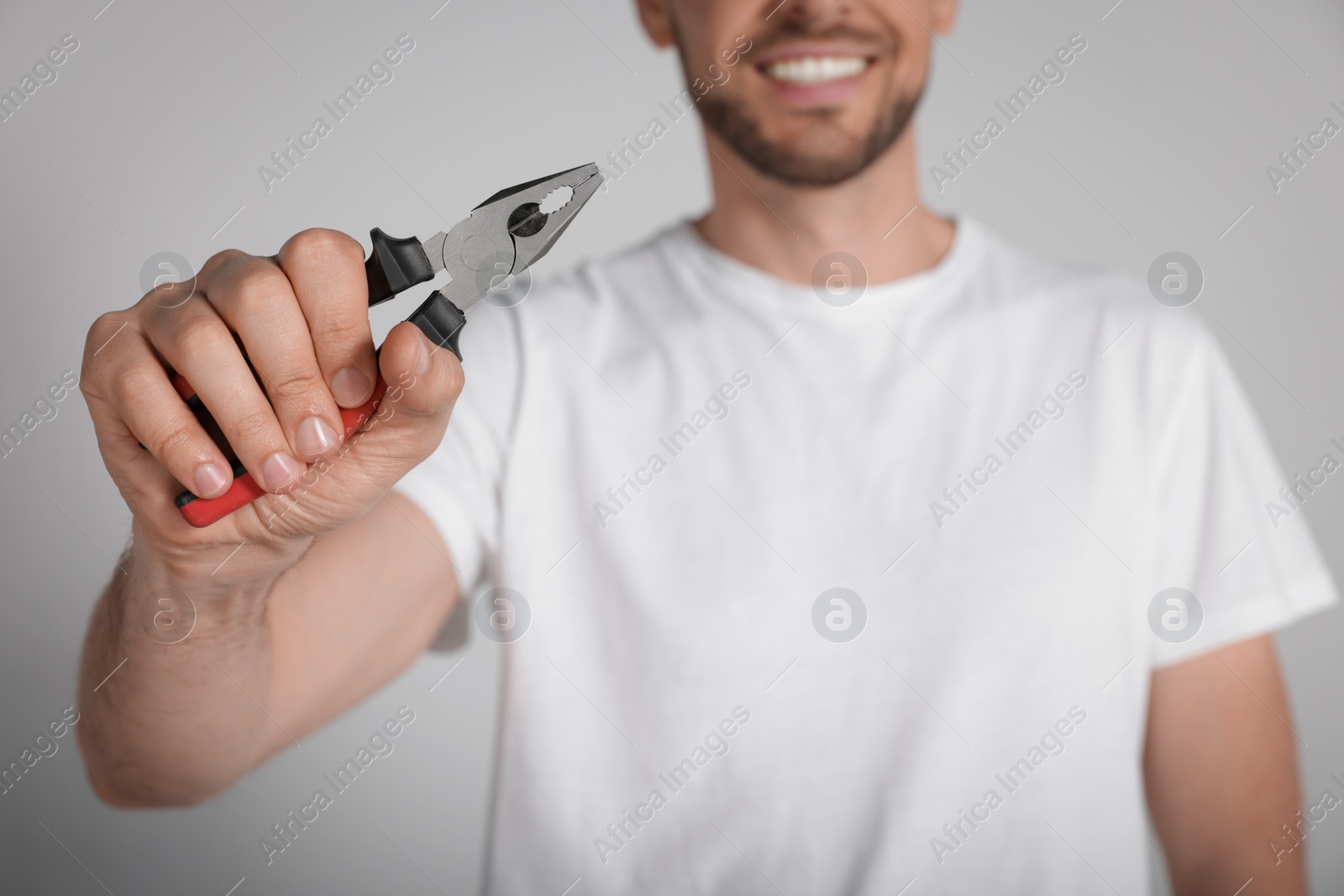 Photo of Happy worker holding pliers on white background, closeup