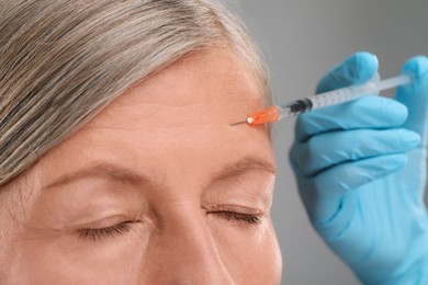 Photo of Doctor giving facial injection to senior woman on light grey background, closeup. Cosmetic surgery