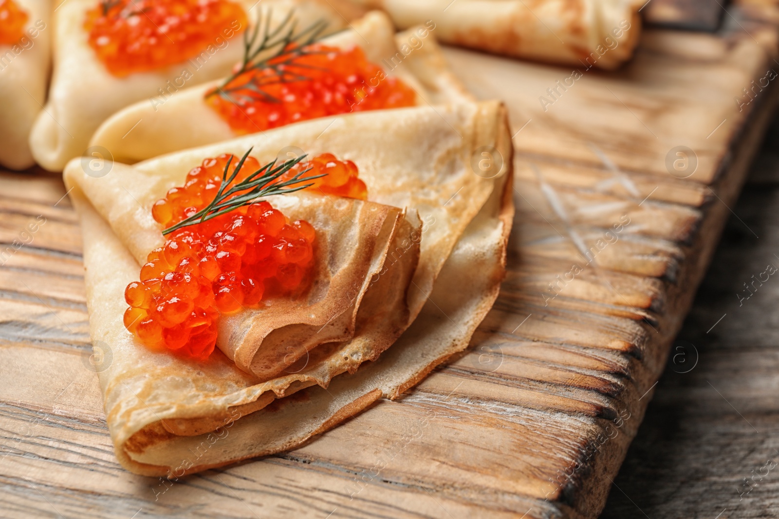 Photo of Thin pancakes with delicious red caviar on wooden board