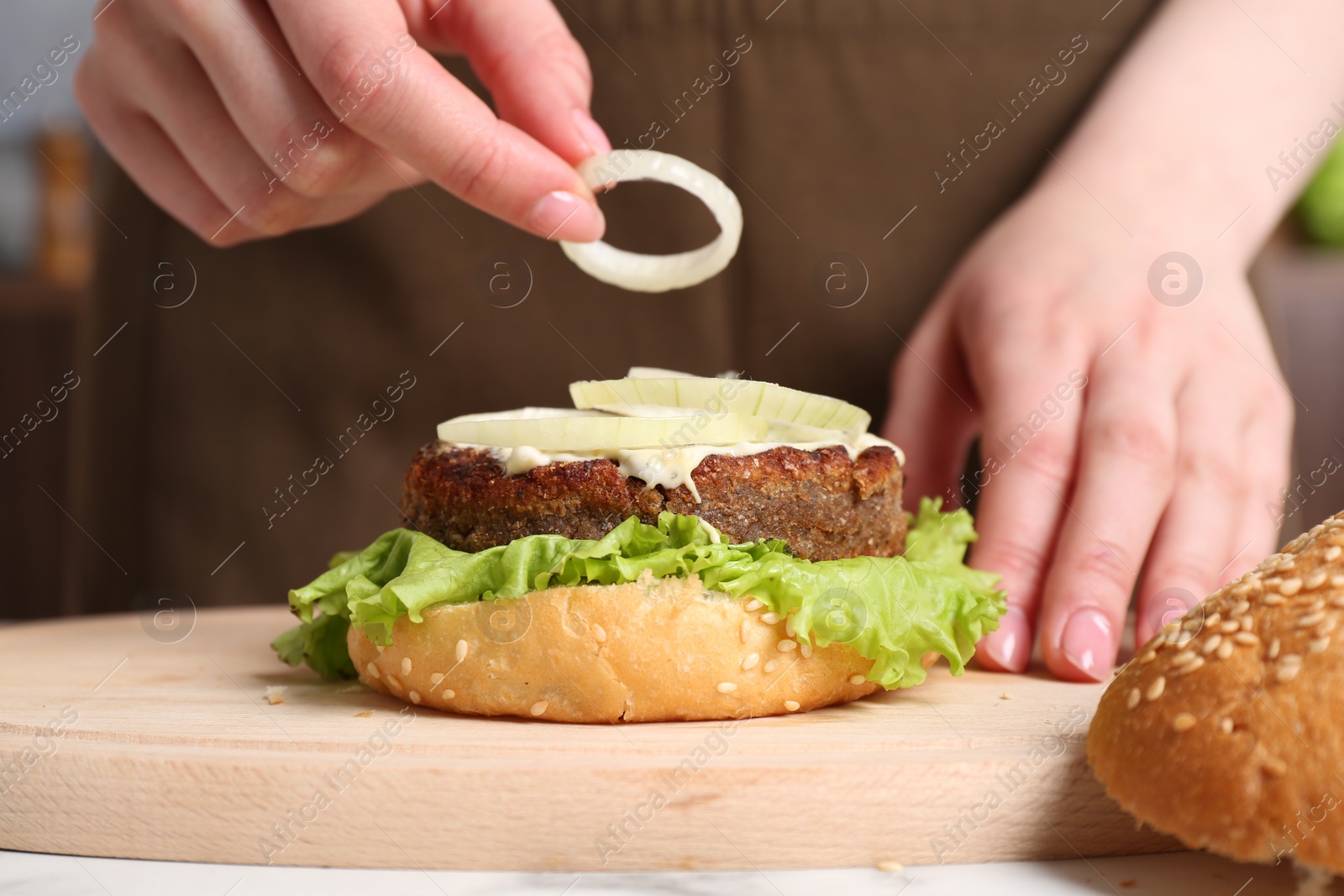 Photo of Woman making delicious vegetarian burger at table, closeup