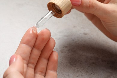 Photo of Woman dripping serum from pipette on her hand at grey table, closeup