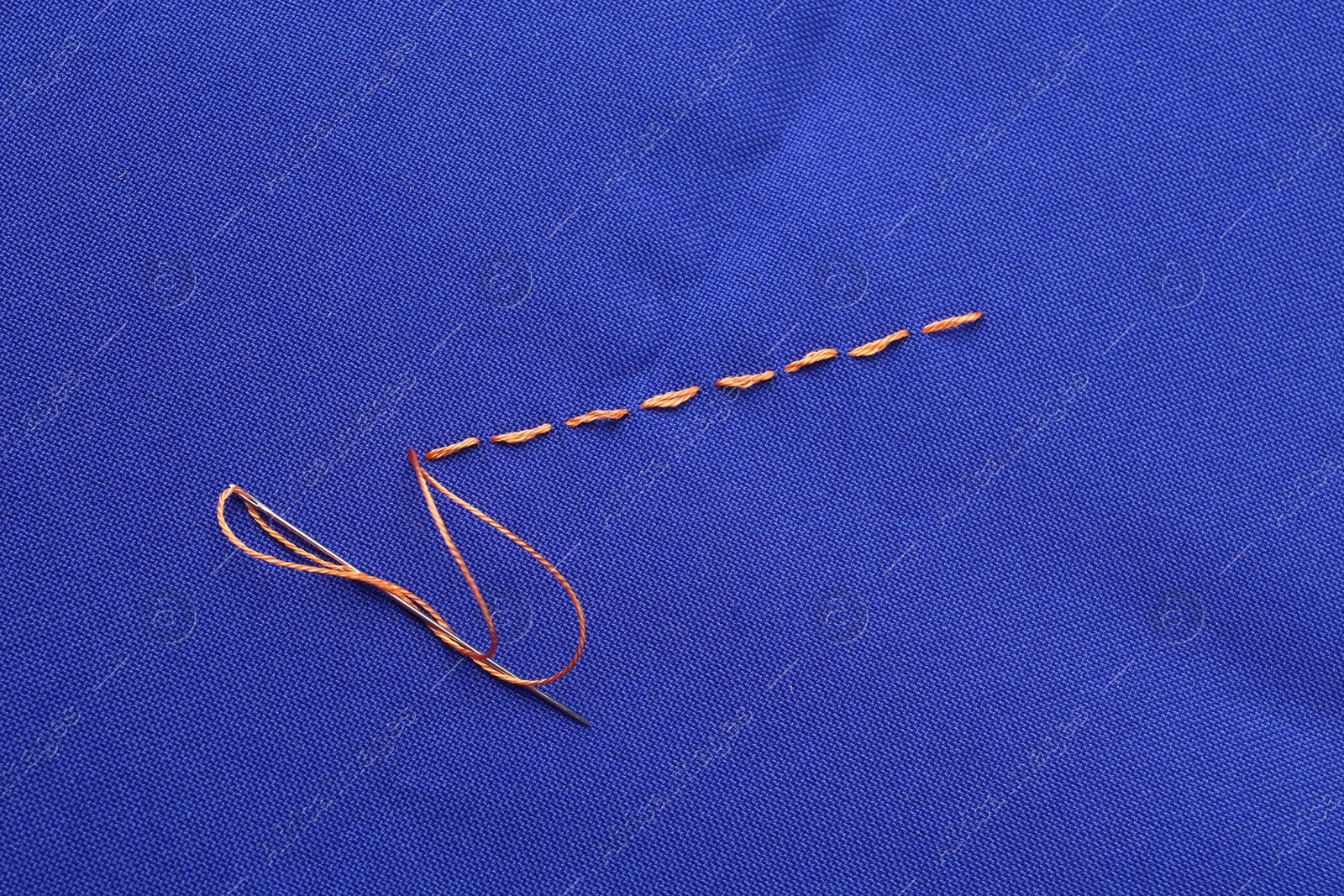 Photo of Sewing needle with thread and stitches on blue cloth, top view