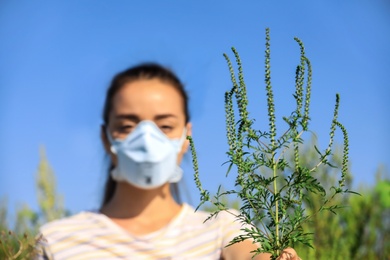 Photo of Young woman with ragweed branch suffering from allergy outdoors, focus on plant