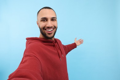 Photo of Smiling young man taking selfie on light blue background, space for text