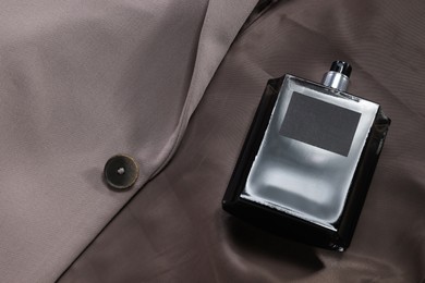 Photo of Luxury men's perfume in bottle on beige jacket, above view. Space for text