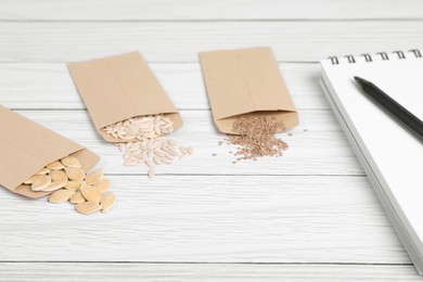 Photo of Many different vegetable seeds and notebook on white wooden table