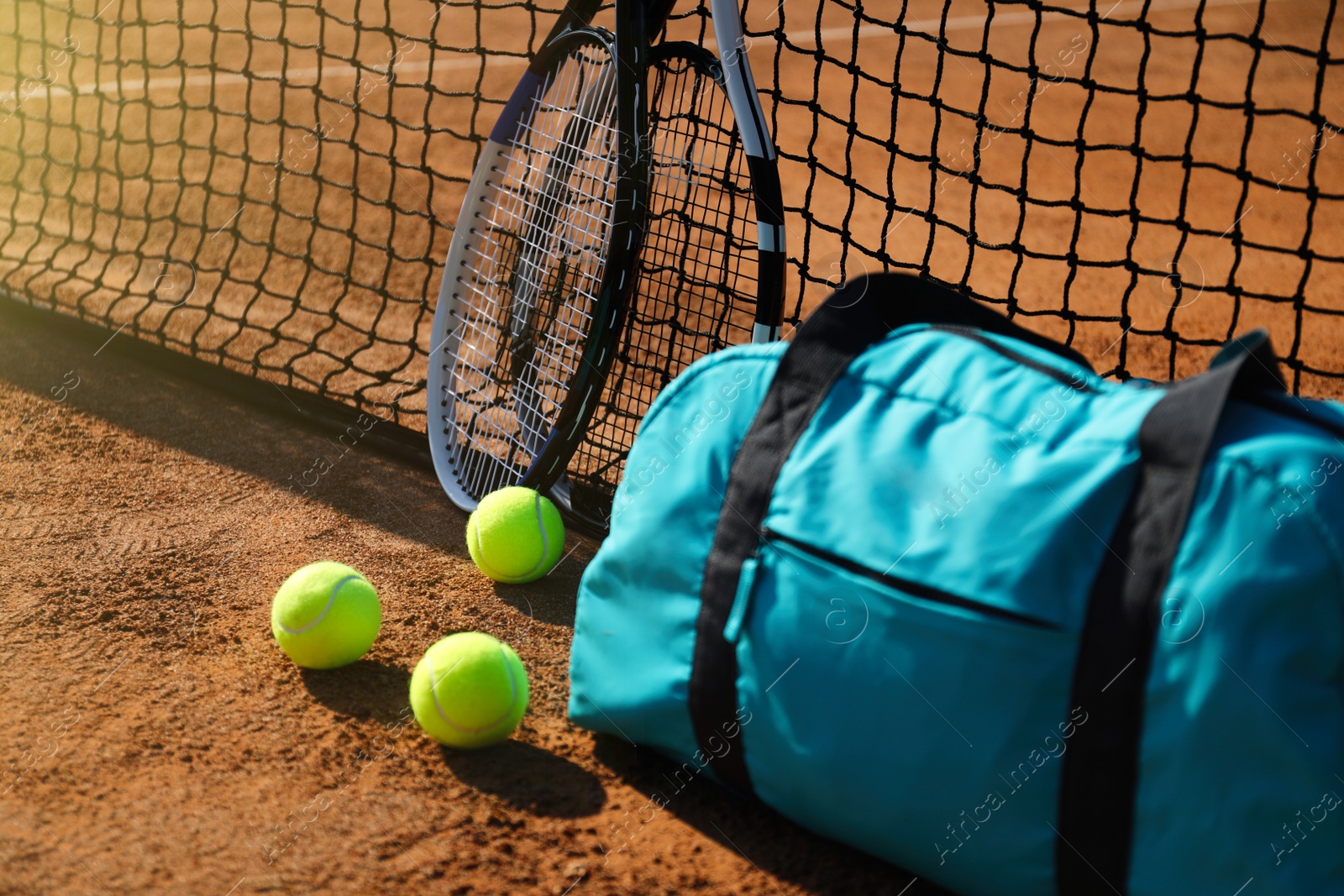 Photo of Tennis balls, rackets and bag near net on clay court