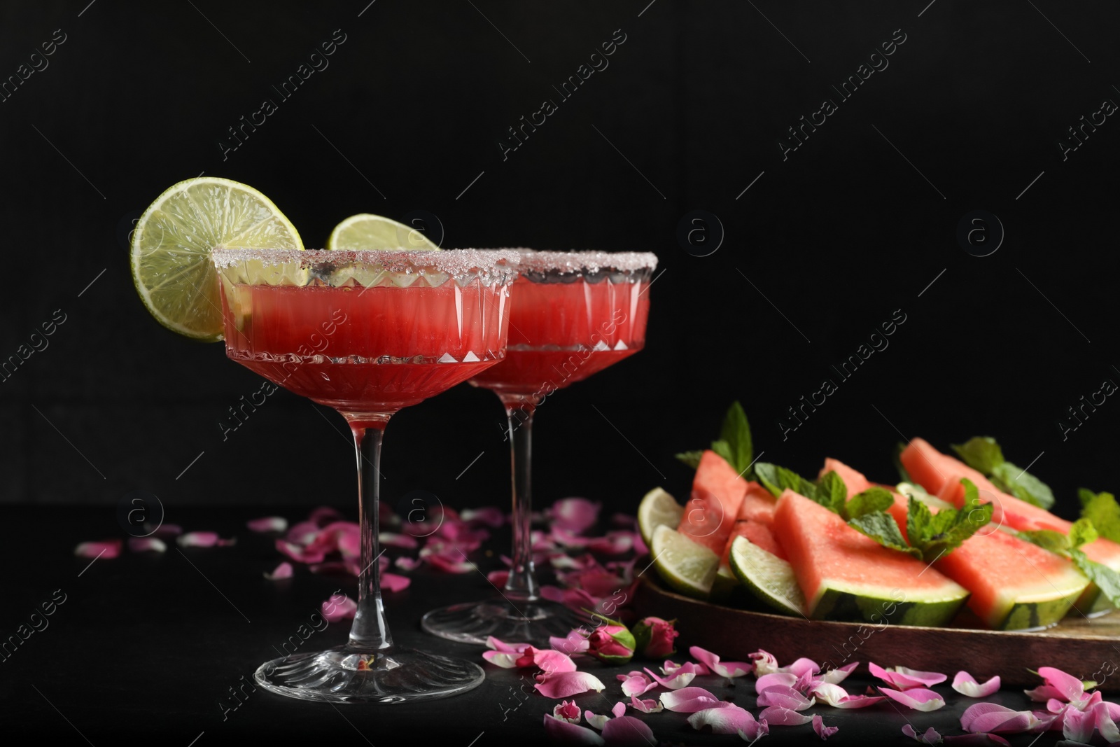 Photo of Cocktail glasses of delicious fresh watermelon juice with lime and rose petals on black table