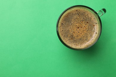 Photo of Aromatic coffee in glass cup on green background, top view. Space for text