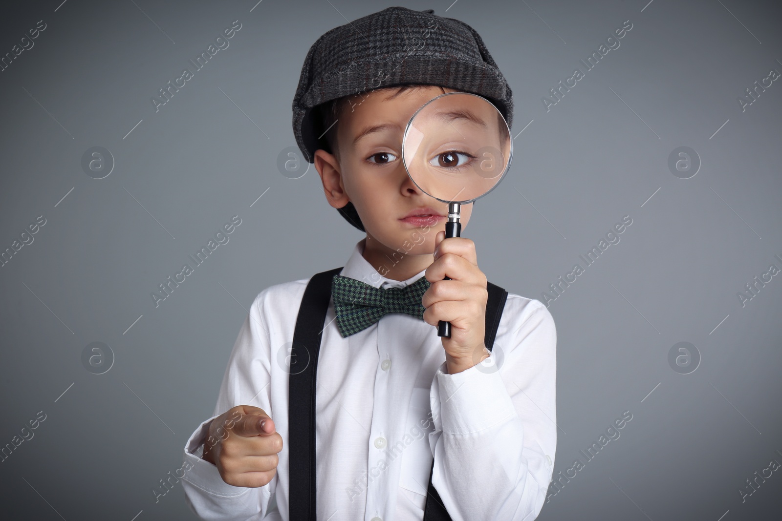 Photo of Little boy with magnifying glass playing detective on grey background