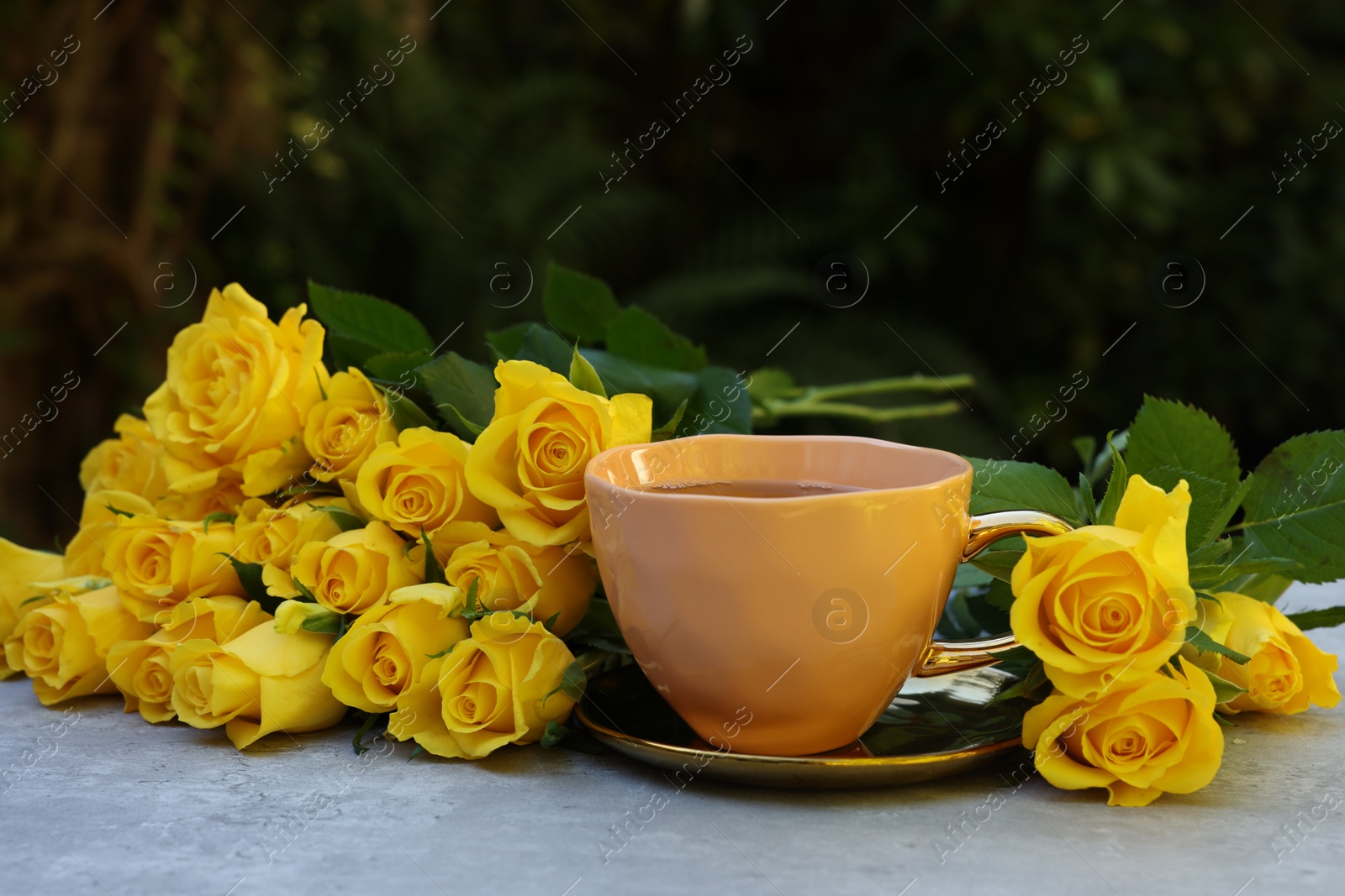 Photo of Cup of drink and beautiful yellow roses on light table outdoors, space for text