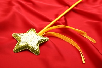 Photo of Beautiful golden magic wand on red fabric, closeup