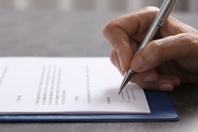 Woman signing document at dark table indoors, closeup