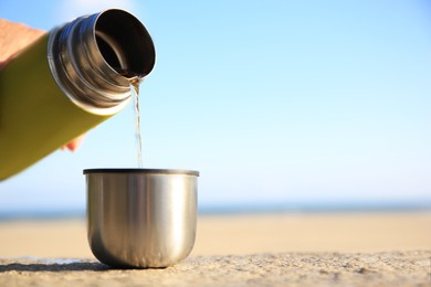 Photo of Woman pouring hot drink from yellow thermos into cap on stone surface outdoors, closeup. Space for text