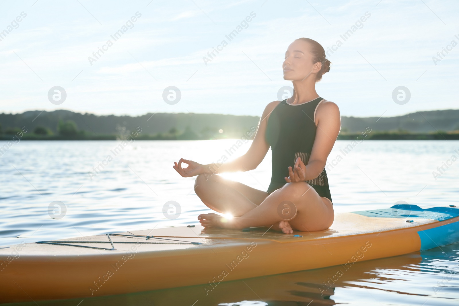 Photo of Young meditating yoga on color SUP board on river at sunset