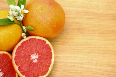 Photo of Fresh ripe grapefruits, flowers and green leaves on wooden table, flat lay. Space for text