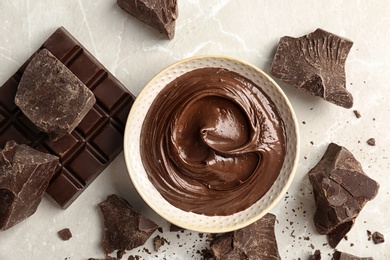 Bowl with tasty melted chocolate and pieces on table, top view