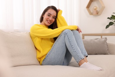 Beautiful young woman in stylish warm sweater on sofa at home