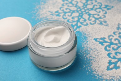Photo of Jar of hand cream and snowflakes on light blue background. Winter skin care