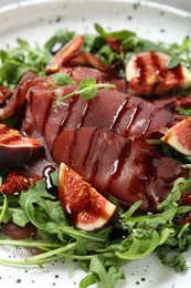 Tasty bresaola salad with figs, sun-dried tomatoes and balsamic vinegar on plate, closeup