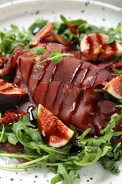 Photo of Tasty bresaola salad with figs, sun-dried tomatoes and balsamic vinegar on plate, closeup