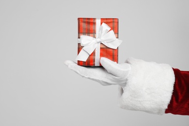 Photo of Santa Claus holding Christmas gift on light grey background, closeup of hand