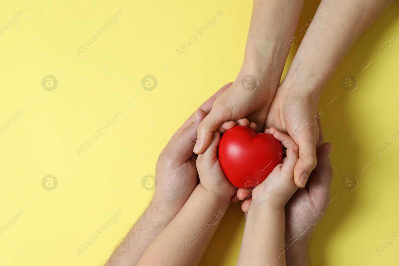 Photo of Parents and child holding red decorative heart on pale yellow background, top view. Space for text