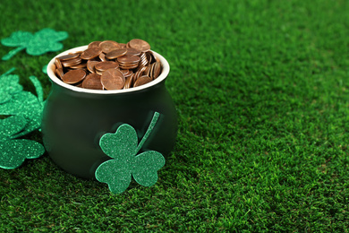 Photo of Pot of gold coins and clover leaves on green grass, space for text. St. Patrick's Day celebration