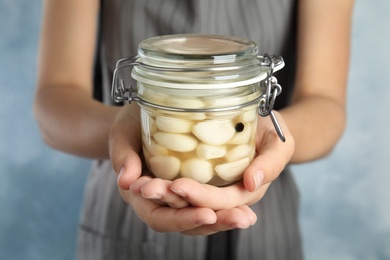 Photo of Woman holding jar with pickled garlic on light background, closeup