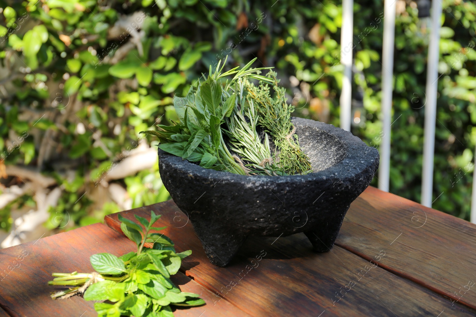 Photo of Mortar with thyme, rosemary and basil on wooden table outdoors. Aromatic herbs